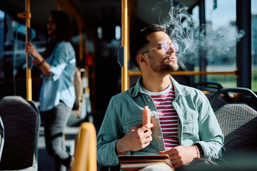 Young man using disposable vape while riding in bus.