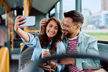 Cheerful couple taking selfie while riding in city bus. © Drazen