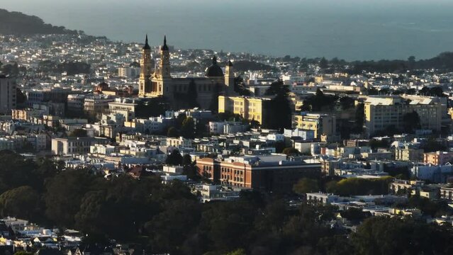 Zoomed aerial shot of Saint Ignatius Church on campus of University of San Francisco. Urban borough and ocean water surface in background.
