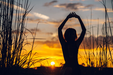 A woman sitting in nature with arms outstretched and enjoying a summertime sunset.