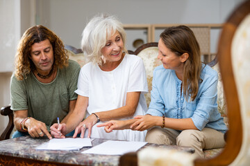 Mature woman at table in home room filling up documents with family