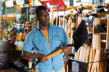 Fototapeta premium Portrait of african american man choosing shovel in gardening market