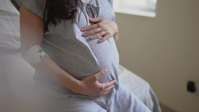 Crop anonymous pregnant female touching tummy in clinic