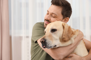 Man hugging his cute Labrador Retriever at home. Space for text