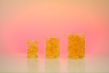Fish oil capsules in transparent flasks on a pink background .Yellow omega oil capsules in...