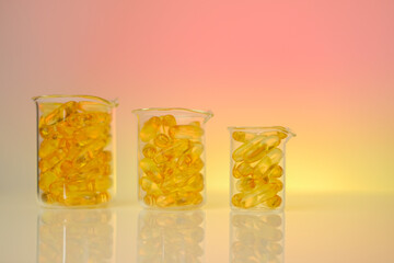 Fish oil falling capsules in transparent flasks on a pink background .Yellow omega fatty acids oil...