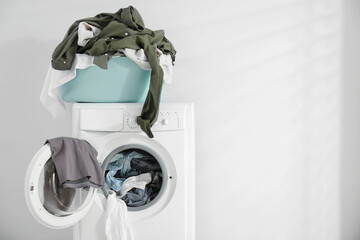 Laundry basket with clothes on washing machine against white background, space for text