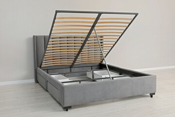 Comfortable bed with storage space for bedding under lifted slatted base in room - obrazy, fototapety, plakaty