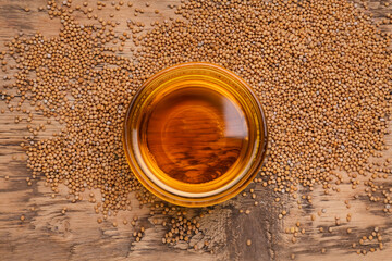 Bowl of natural oil and mustard seeds on wooden table, top view