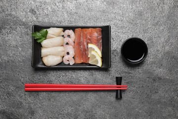 Sashimi set served with soy sauce, lemon and parsley on light grey table, flat lay