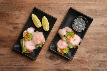 Tasty spring rolls served with lime and soy sauce on wooden table, flat lay