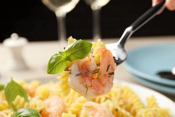 Woman eating delicious pasta with shrimps and basil, closeup
