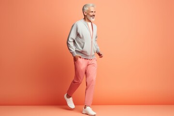 Fototapeta na wymiar full length view of smiling senior man in sweatshirt and pink pants walking on orange