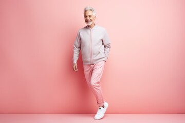 Fototapeta na wymiar full length of smiling senior man in pink tracksuit standing on pink
