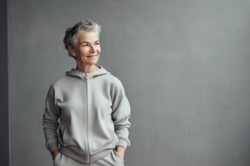 Portrait of smiling senior woman in grey hoodie standing against grey wall