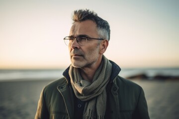 Fototapeta premium Portrait of a handsome middle-aged man with glasses and a scarf on the beach.