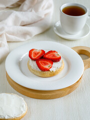 Tasty bruschetta with cream cheese and slices of ripe strawberries on white plate with cup of tea on white background. Side view, close up, vertical