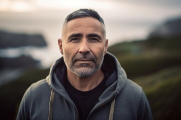 Fototapeta premium Portrait of a handsome middle-aged man with grey hair, wearing a gray sweatshirt, standing on a hill, looking at the camera.