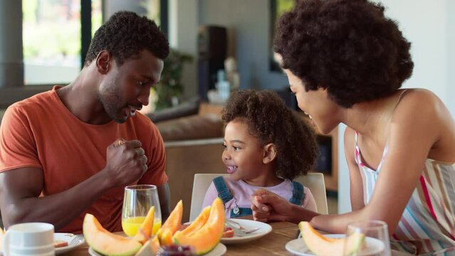 Family having breakfast with parents and daughter around table at home playing rock paper scissors before eating melon - shot in slow motion