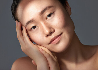 Her skin looks soft, supple and radiant. Studio shot of a beautiful young woman posing against a grey background.