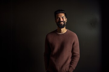 Portrait of a happy young man with a beard in a sweater on a dark background