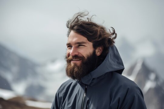 Handsome young man with long beard and moustache in blue jacket on snowy mountain top
