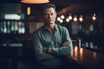 Fototapeta premium Portrait of handsome mature man standing with arms crossed in pub.