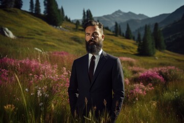 Naklejka na ściany i meble Handsome bearded man with long beard and mustache in black suit standing on mountain meadow.