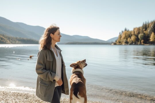 Young woman walking her dog on the shore of a mountain lake.