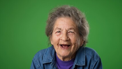 Funny crazy closeup portrait of happy laughing elderly senior old woman with wrinkled skin and grey hair on green screen background.