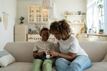 Pensive African American small boy touch virtual reality glasses for smartphone together with...