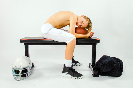 Youth male football player asleep shirtless on bench with his head resting on a football - Powered by Adobe