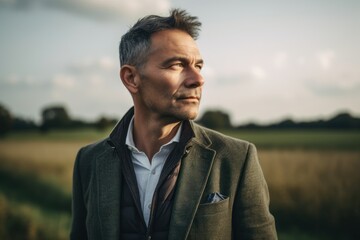 Lifestyle portrait photography of a grinning man in his 40s wearing a classic blazer against a countryside or rural background. Generative AI