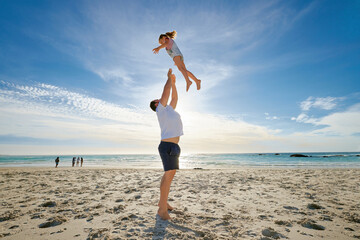 Father lifting daughter, having fun on the beach. A smiling young man playing with his cute little girl on vacation. Fun family vacation