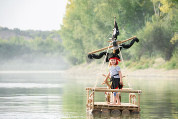 Child in a pirate costume plays on a wooden raft at sunset. Girl pretends to be the captain of a...