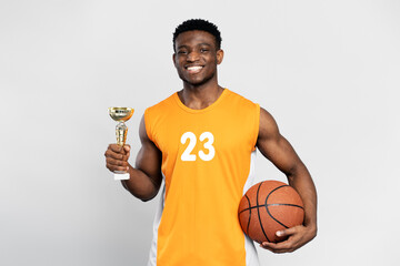 Confident smiling African man, basketball player holding trophy cup and ball, celebration success...