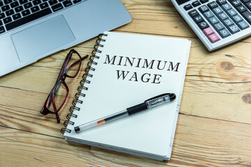 Minimum wage text on notepad with calculator and laptop.