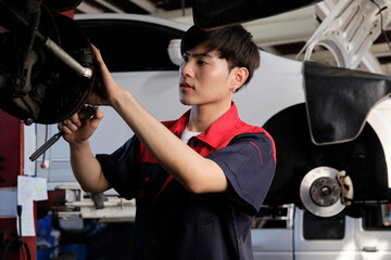 One young expert Asian male automotive mechanic technician is screwing car wheel nuts on lifting with wrench for repair at garage. Vehicle maintenance service works, industry occupation business jobs.