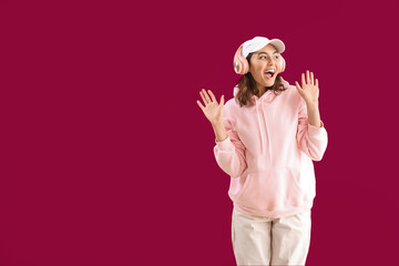 Surprised young woman in headphones on pink background