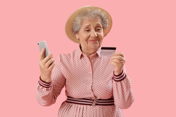 Senior woman with mobile phone and credit card on pink background - Powered by Adobe