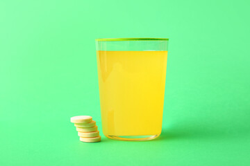 Glass of effervescent tablet dissolved in water on green background