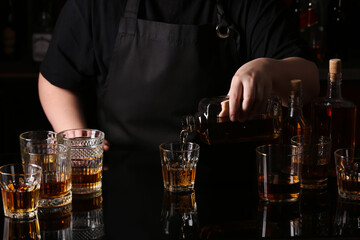 Woman pouring tasty rum from bottle into glasses at table in bar, closeup