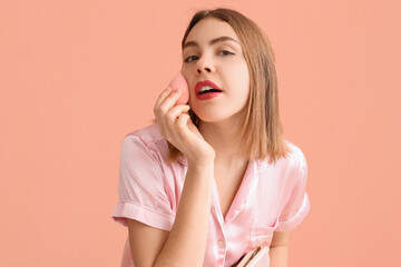Young woman with cosmetic bag and makeup sponge on pink background, closeup
