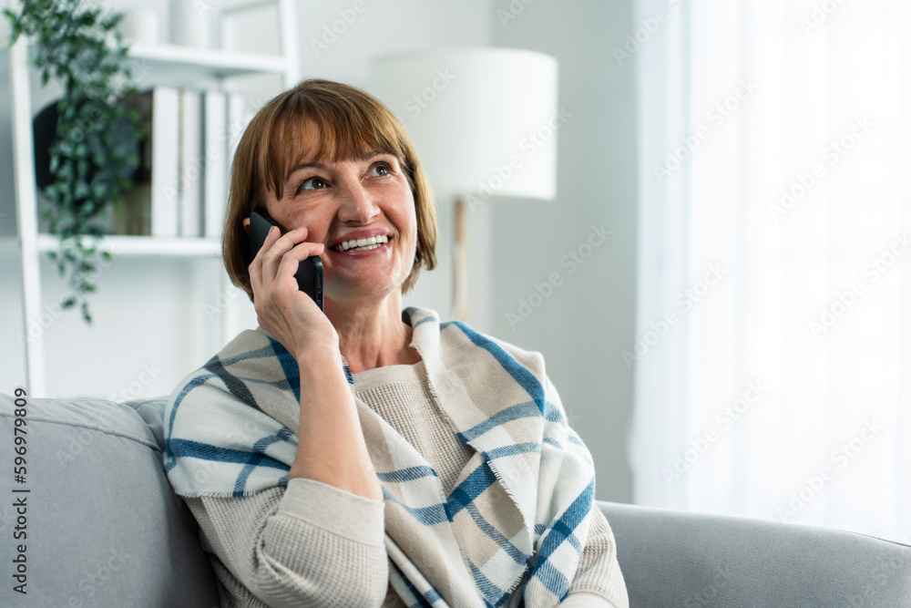 Wall mural senior elderly woman sit on sofa and talking on mobile phone in house.