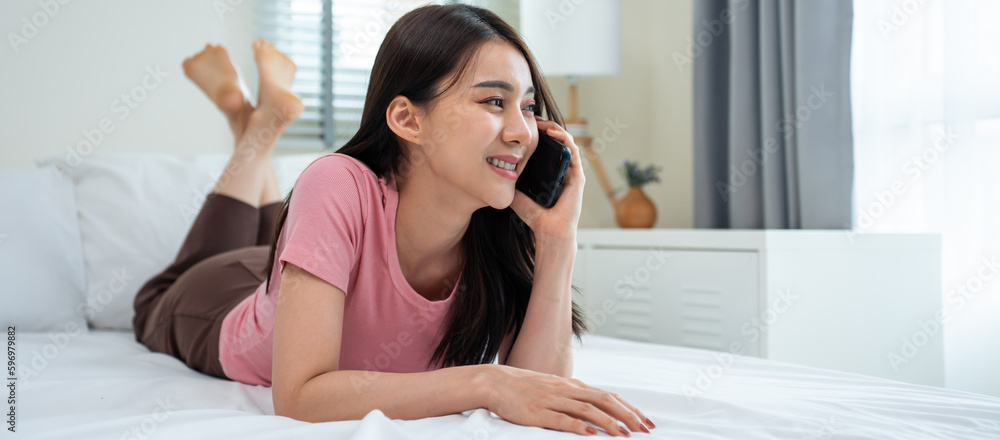 Wall mural Asian attractive woman use mobile phone chat on bed at home in morning. 