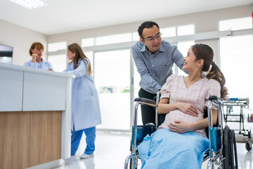 Obraz premium Asian husband taking care of pregnant woman sitting on wheelchair. 