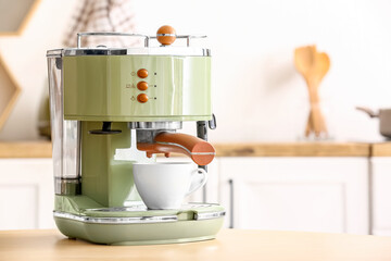 Modern coffee machine with cup on wooden table in kitchen