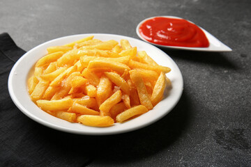 Plate with tasty french fries and ketchup on dark background, closeup