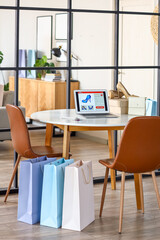 Laptop with open page of online store, mobile phone and credit card on table in room