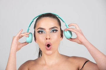 Fototapeta premium Excited young woman listen music with headphones, dancing. Girl listening to music using wireless earphones isolated over studio background.